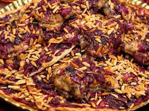 A tray of mosakhan close up: chicken pieces under onions with sumac and toasted almonds