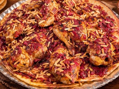 Roast chicken on taboon bread in a round tray, topped with sumac onions and almonds